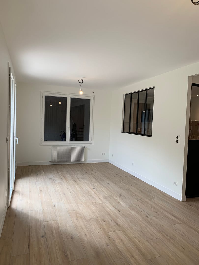 Perspective large du séjour d’un pavillon à Saint Maur avec un parquet chêne lumineux, offrant une sensation d’ouverture et de fluidité dans la maison.