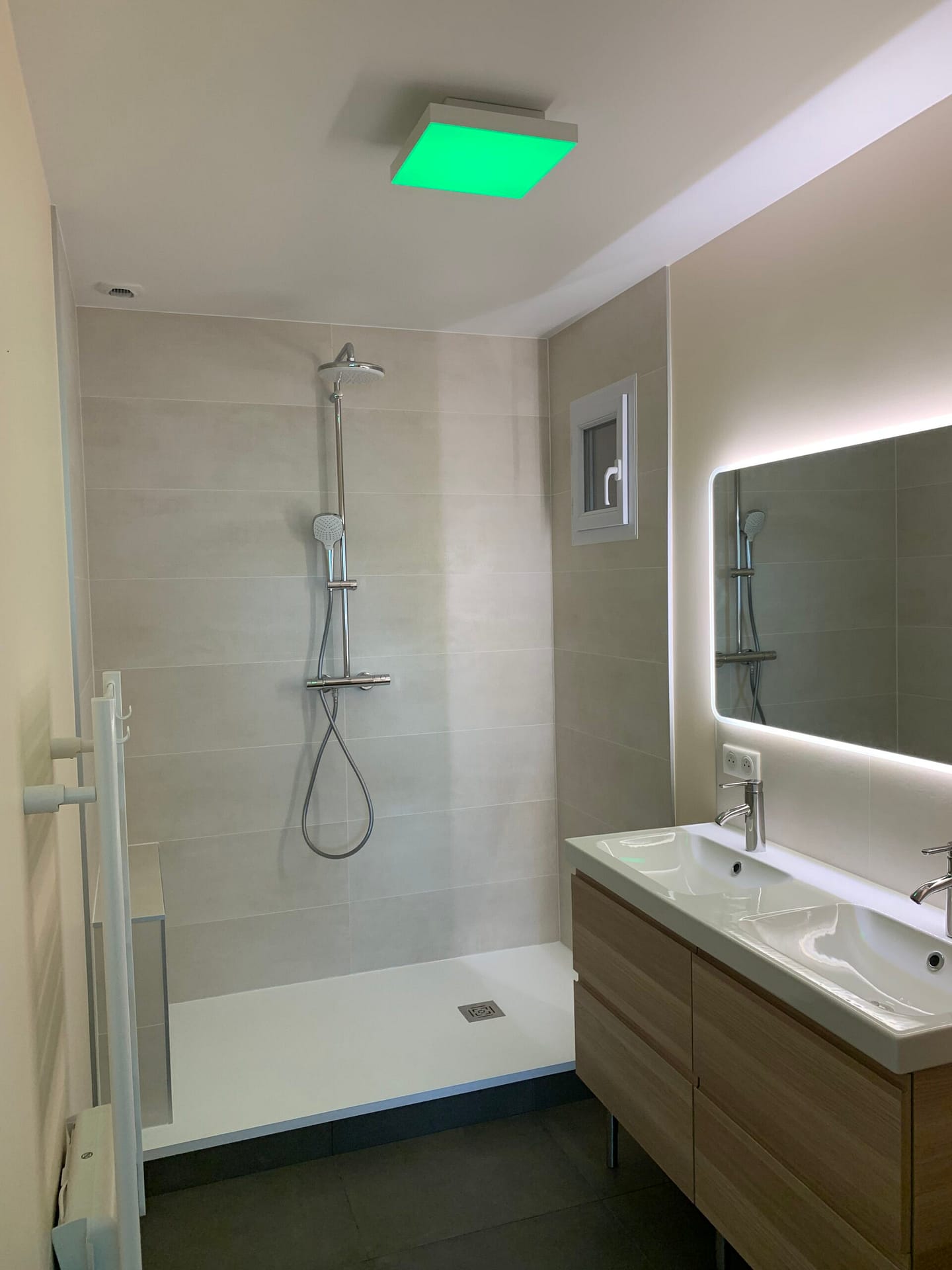 Salle de bains moderne avec éclairage encastré, miroir éclairé et meuble vasque en bois à Ozoir la Ferrière, réalisée par Design & Couleurs.
